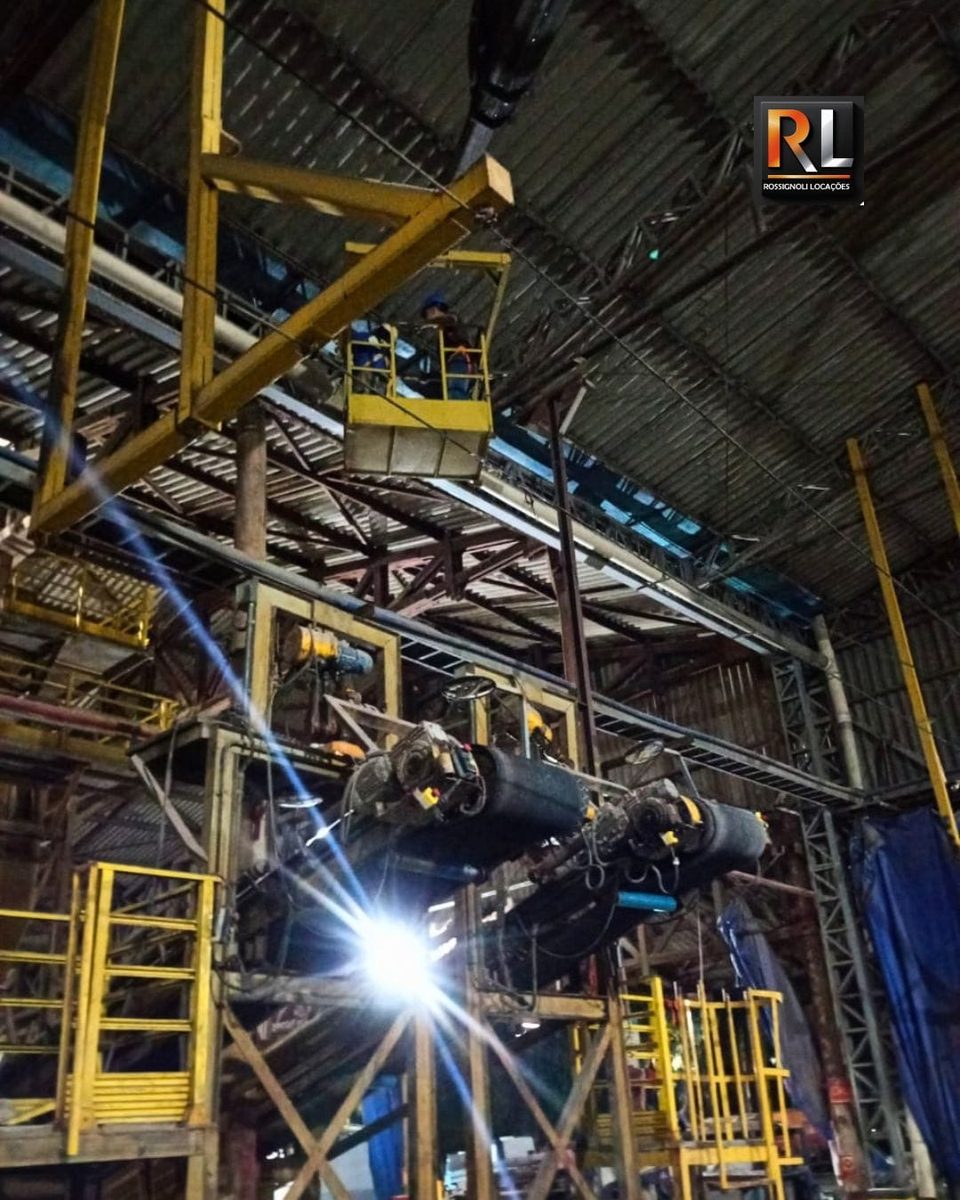 Profissional no cesto aéreo do munck fazendo manutenção no alto de uma indústria